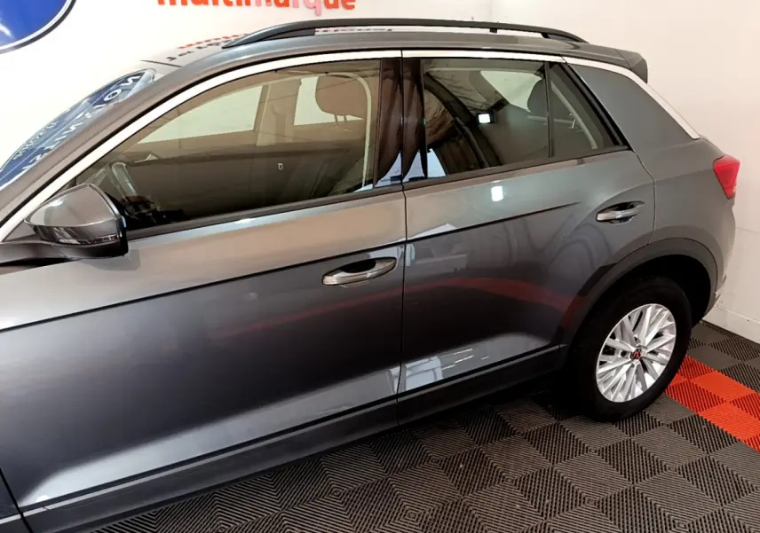 Profil côté gauche d'un Volkswagen T-Roc gris foncé, mettant en valeur les jantes et les rétroviseurs noirs avec clignotants intégrés.