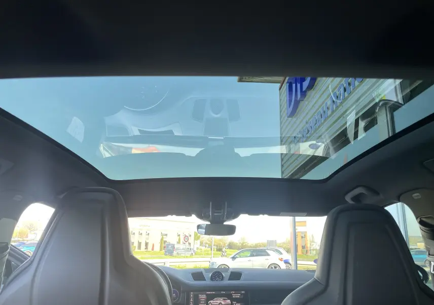 Vue intérieure du Porsche Cayenne Coupé E-Hybrid noir 2021, mettant en valeur le toit panoramique et les sièges avant en cuir.