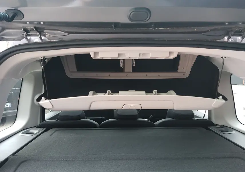 Vue intérieure arrière du coffre ouvert du Peugeot Rifter gris platinium, montrant la tablette arrière relevée et les sièges arrière noirs.
