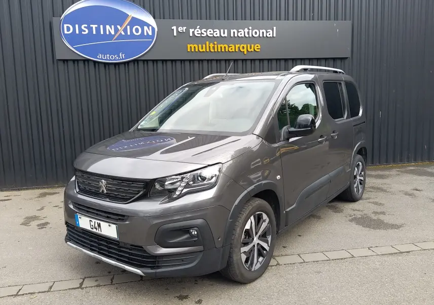 Peugeot Rifter gris platinium en 3/4 avant droit, avec jantes alliage et barres de toit visibles.