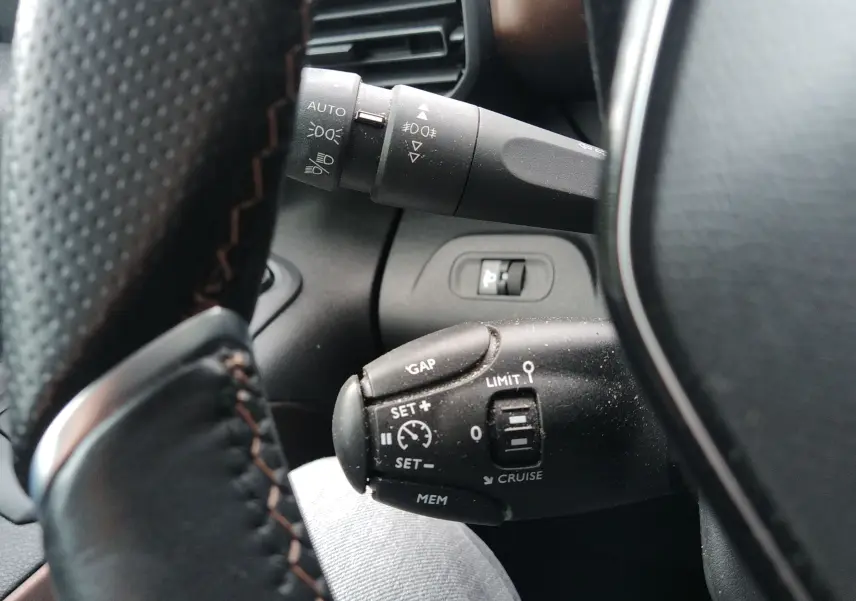 Gros plan sur les commandes au volant du Peugeot Rifter 1.5 BlueHDI 130ch GT, avec boutons de régulateur de vitesse et éclairage.