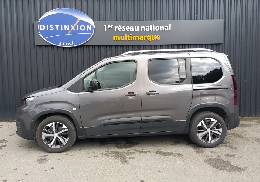 Vue de profil côté gauche d’un Peugeot Rifter gris platinium 2022 avec jantes alliage et barres de toit.