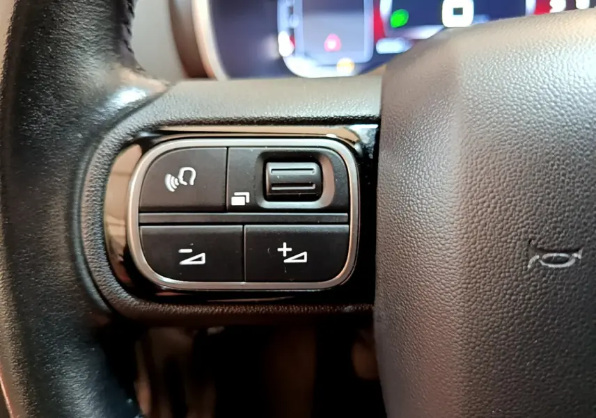 Gros plan sur les commandes gauche du volant cuir noir du Citroën C5 Aircross 2020, avec tableau de bord numérique flou.