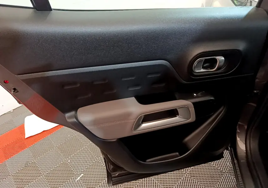 Vue rapprochée de la porte arrière gauche du Citroën C5 Aircross gris foncé, avec accoudoir clair et poignée intégrée.