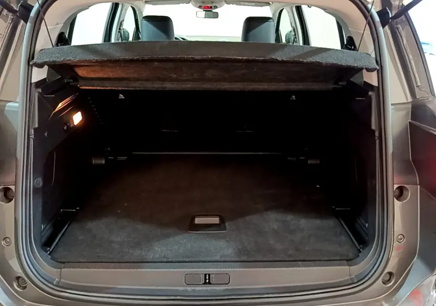 Coffre ouvert vu de l'arrière d'un Citroën C5 Aircross gris foncé avec cache-bagages relevé et éclairage intérieur allumé.