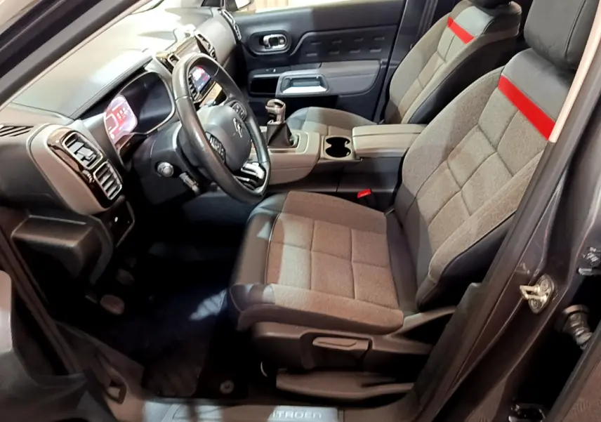 Intérieur avant droit du Citroën C5 Aircross gris foncé, sièges tissu gris avec bande rouge et volant cuir noir.