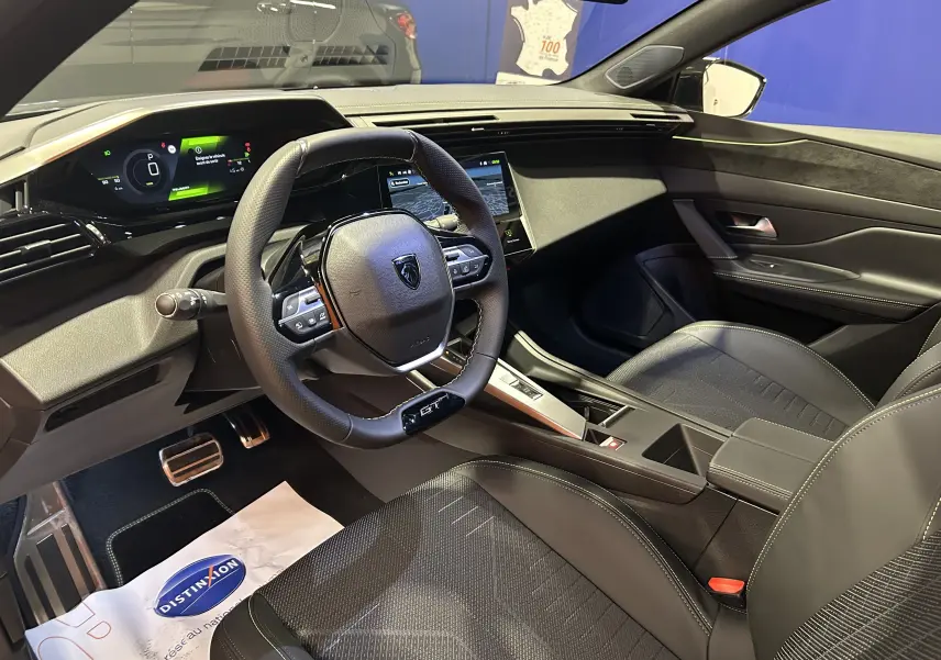 Vue intérieure côté conducteur de la Peugeot 308 gris Selenium, avec volant GT et tableau de bord numérique 3D.