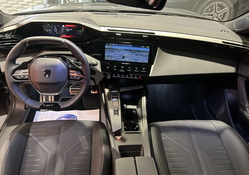 Vue intérieure avant de la Peugeot 308 III Ph.2 HYBRID 145 GT, tableau de bord numérique et écran central GPS.