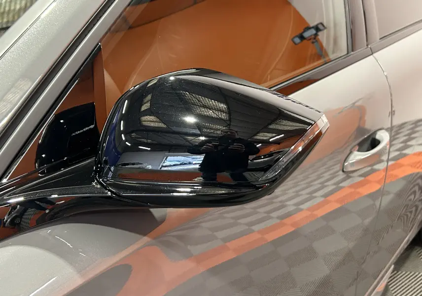 Rétroviseur noir côté gauche d’une Peugeot 308 gris Selenium, vue rapprochée sur la portière avant.