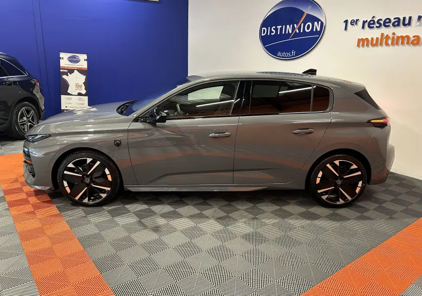 Profil droit de la Peugeot 308 III Ph.2 HYBRID 145 GT gris Selenium, avec jantes noires et détails modernes en showroom.