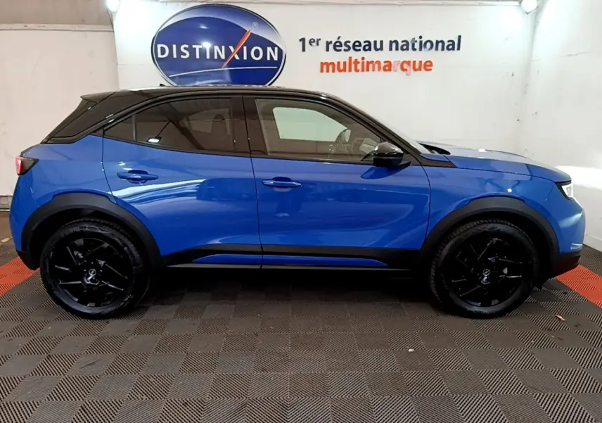 Profil latéral droit d'un Opel Mokka 1.2 Turbo 136ch GS bleu avec toit noir et jantes noires dans un showroom.