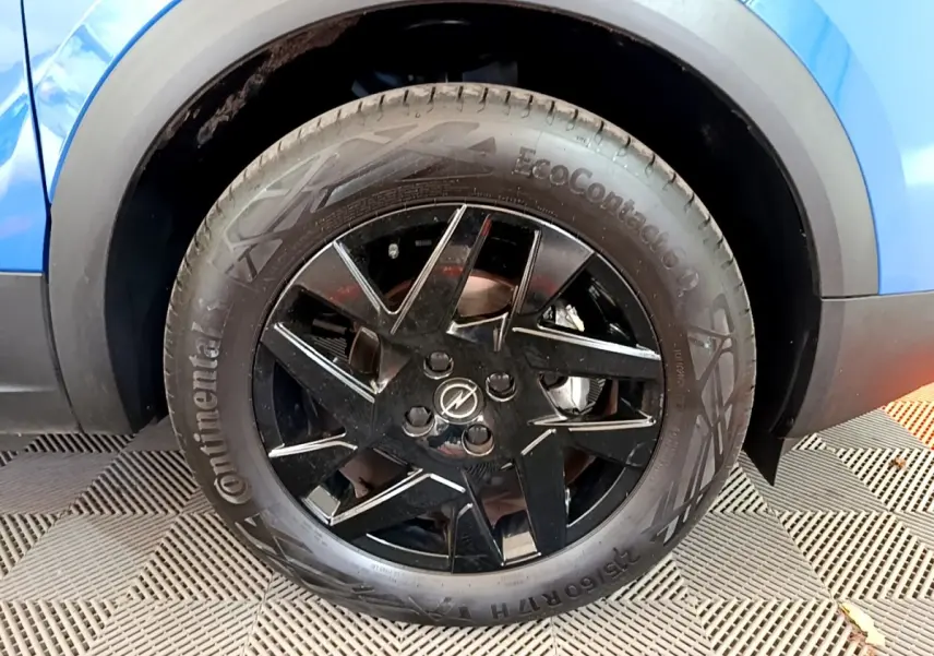 Gros plan sur la roue avant droite noire brillante d’un Opel Mokka bleu 2024 avec jante en alliage.