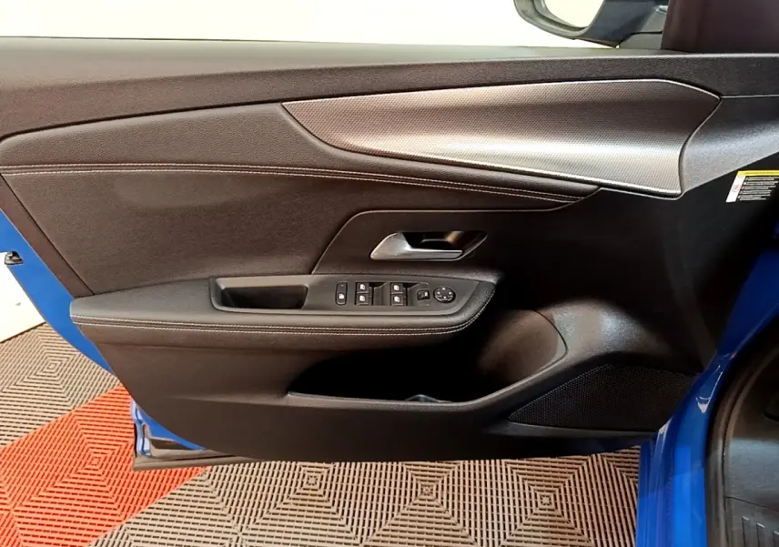 Vue intérieure côté gauche de la porte avant bleue de l’Opel Mokka 2024 avec commandes de vitres et poignée argentée.