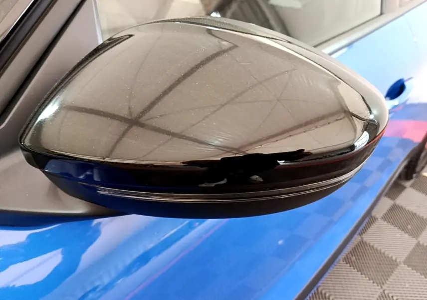 Rétroviseur côté gauche noir brillant sur Opel Mokka bleu, vue rapprochée avec reflet de la structure environnante.