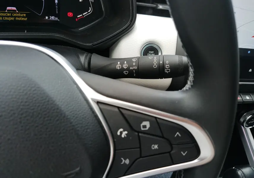 Gros plan sur le volant et la commande d’essuie-glace de la Renault Clio V E-TECH orange, intérieur noir et blanc.