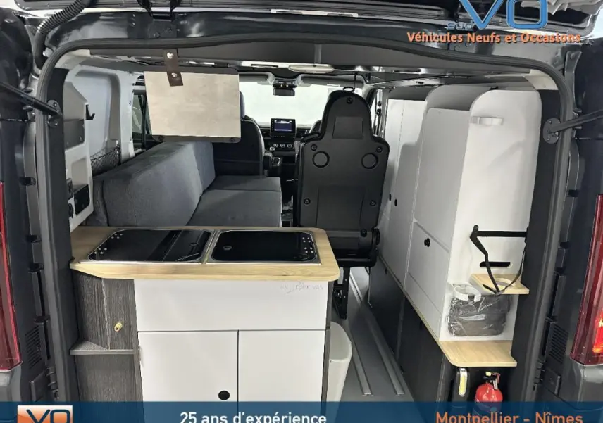 Vue arrière intérieure du Renault Trafic Fourgon gris 2025 aménagé avec kitchenette et banquette grise.