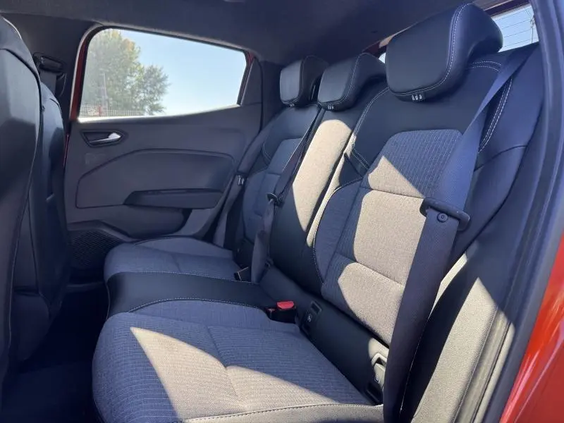 Vue latérale droite de l’habitacle arrière de la Renault Clio orange 2025, sièges tissu gris avec ceintures noires.