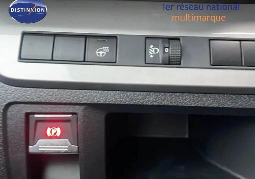 Détail intérieur du tableau de bord du Citroën Jumpy gris titane, montrant les commandes de réglage des phares et frein à main électrique.