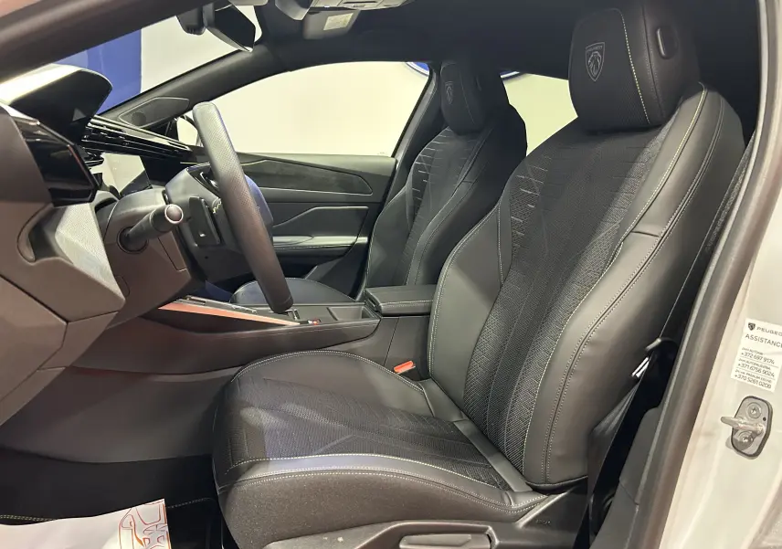 Vue intérieure côté conducteur de la Peugeot 308 III Ph.2 HYBRID 145 GT avec sièges cuir et logo Peugeot brodé sur appuie-tête.