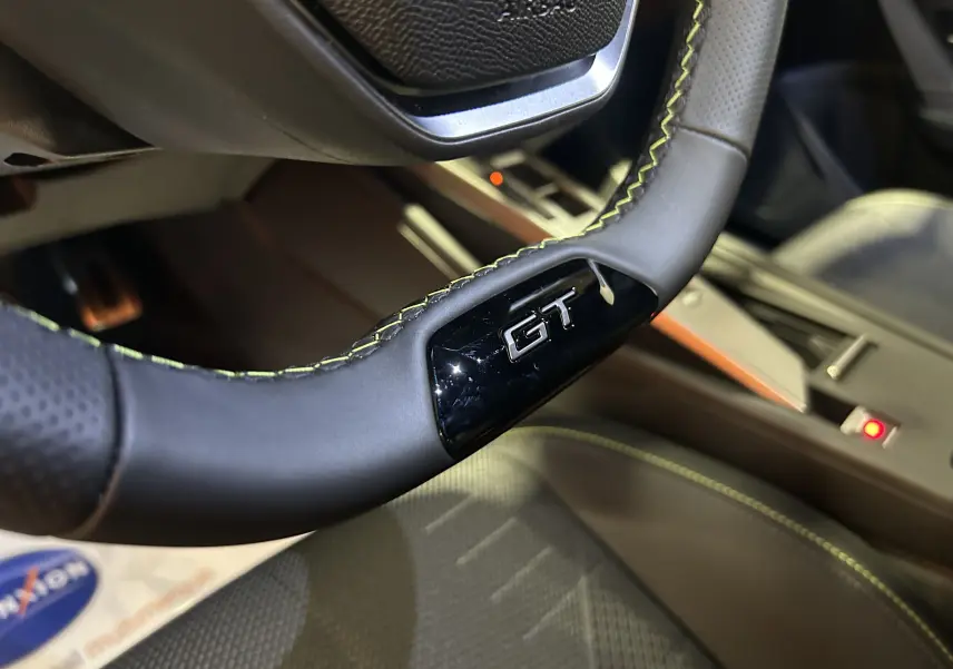 Gros plan sur le volant GT avec surpiqûres jaunes et partie intérieure cuir perforé du Peugeot 308 Hybrid 2026.