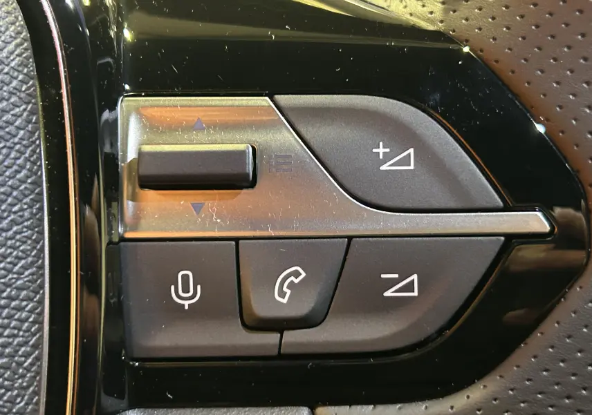 Gros plan sur les commandes vocales et téléphone sur le volant en cuir perforé du Peugeot 308 blanc Okenite.
