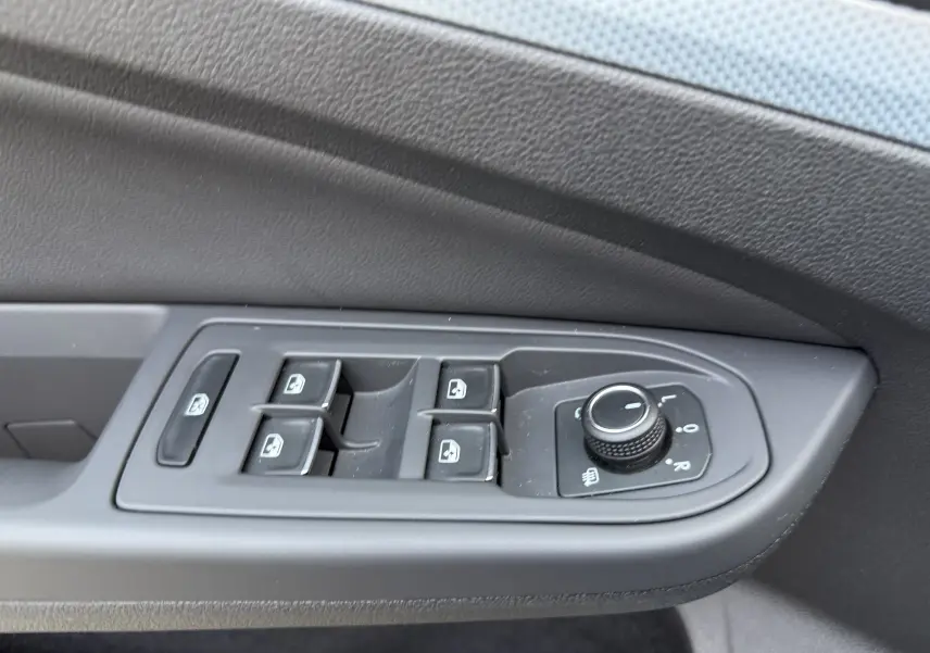Détail des commandes de lève-vitres et réglage des rétroviseurs sur la porte côté gauche d’un Volkswagen Golf SW gris lunaire.