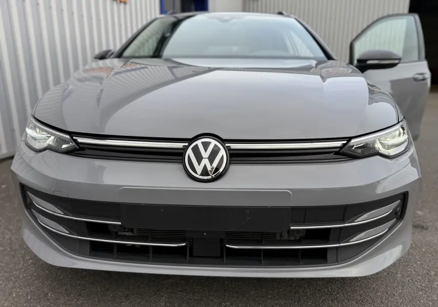 Vue frontale rapprochée d’une Volkswagen Golf SW gris lunaire 2025 avec phares allumés et porte avant droite ouverte.