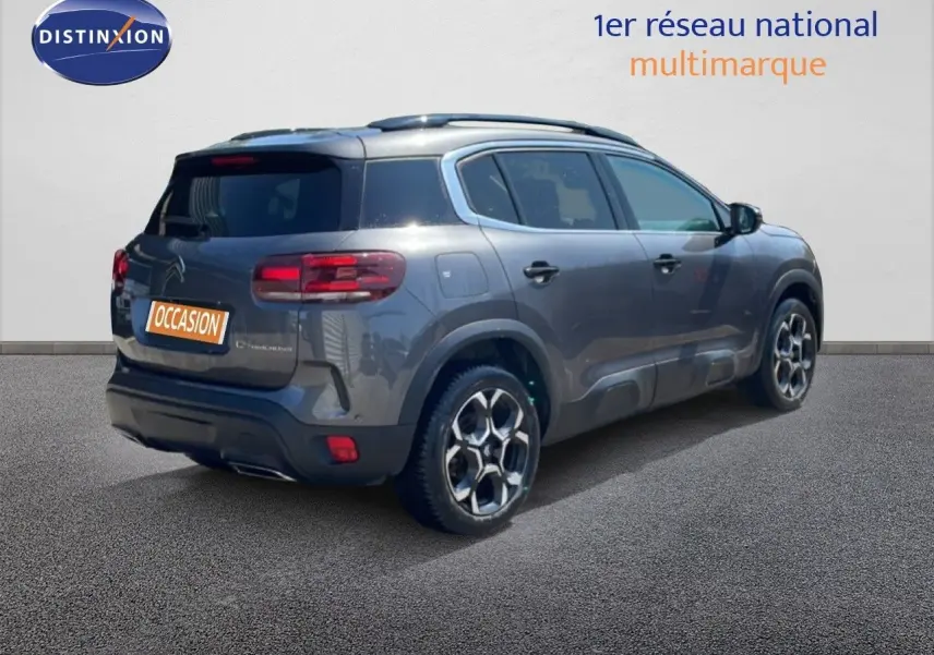 Vue 3/4 arrière droite d'un Citroën C5 Aircross gris platinium métallisé avec jantes bi-ton et barres de toit.