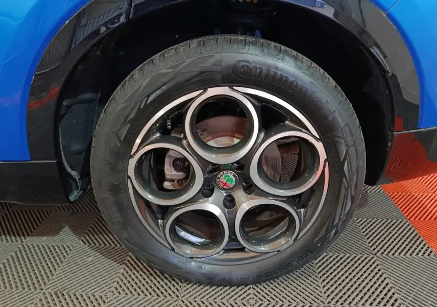 Gros plan sur la roue avant droite d'une Alfa Romeo Tonale bleu, avec jante distinctive à cinq cercles.