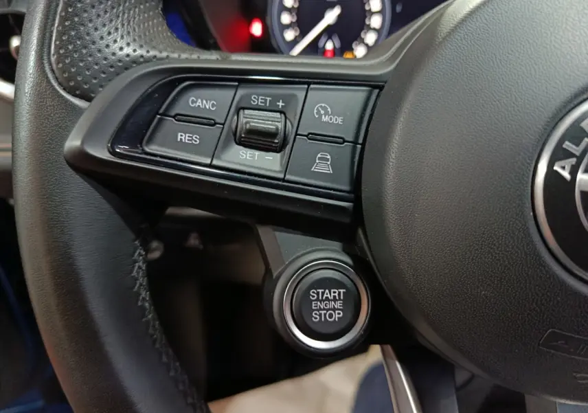 Gros plan sur le volant noir de l'Alfa Romeo Tonale avec les commandes de régulateur et le bouton start engine stop.