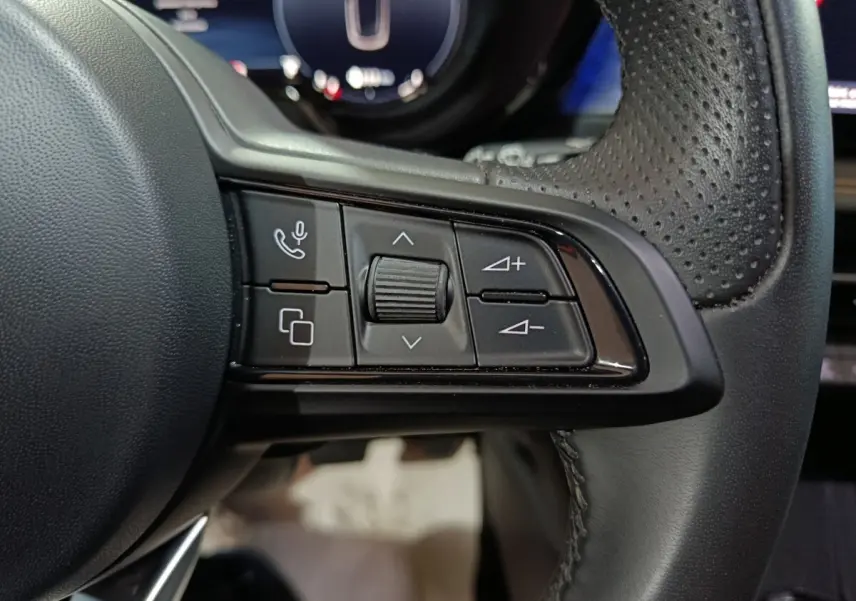 Gros plan sur les commandes multifonctions à gauche du volant en cuir perforé de l'Alfa Romeo Tonale bleu.