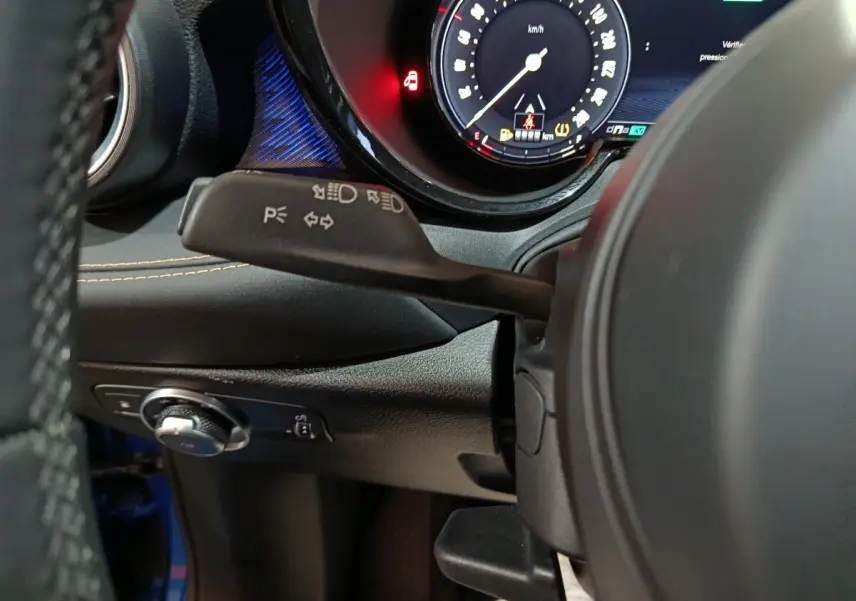 Gros plan intérieur sur le volant et le combiné d'instruments numérique de l'Alfa Romeo Tonale bleu, avec commandes et éclairage ambiant.