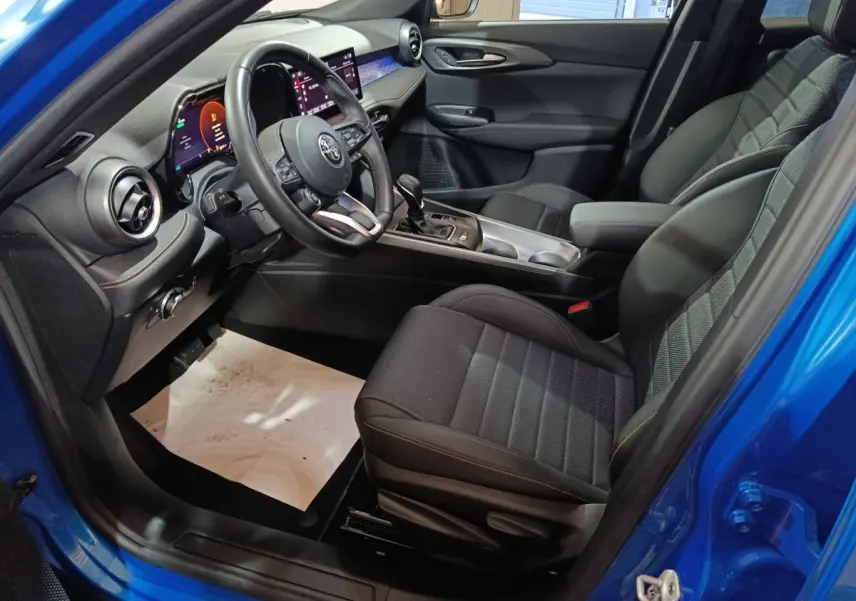 Vue intérieure côté conducteur de l'Alfa Romeo Tonale bleu, montrant sièges noirs et tableau de bord digital moderne.