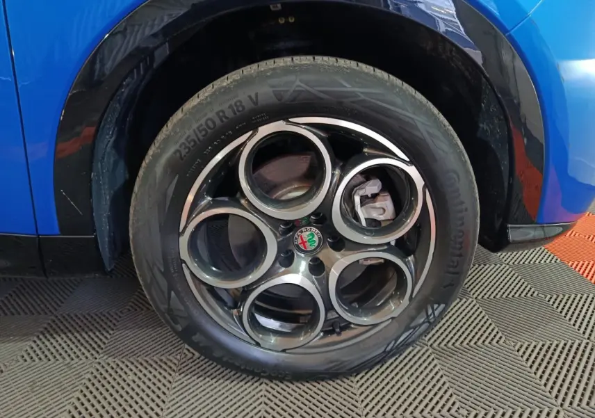 Gros plan sur la roue avant gauche d'une Alfa Romeo Tonale bleu, avec jante distinctive à cinq cercles.