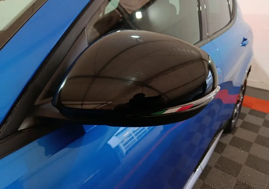 Gros plan sur le rétroviseur droit noir brillant avec drapeau italien, sur la portière bleue de l'Alfa Romeo Tonale 2023.