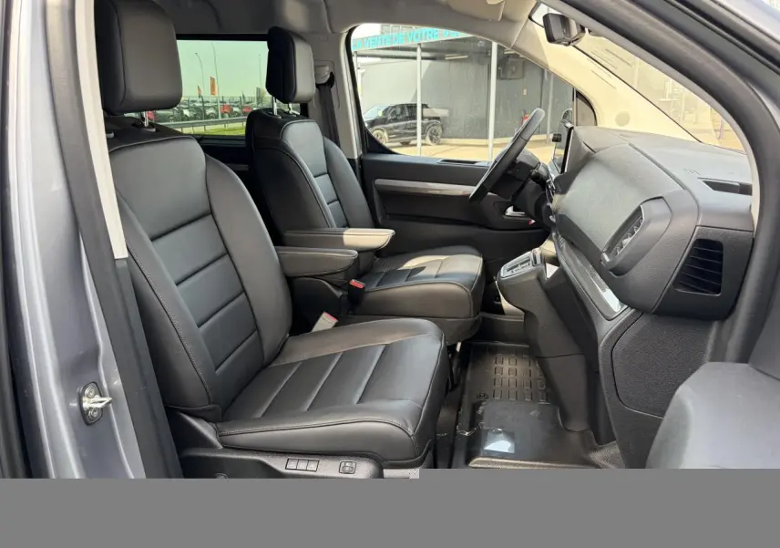 Vue intérieure côté gauche du Citroën Jumpy gris acier, montrant les sièges avant en cuir noir avec accoudoirs.