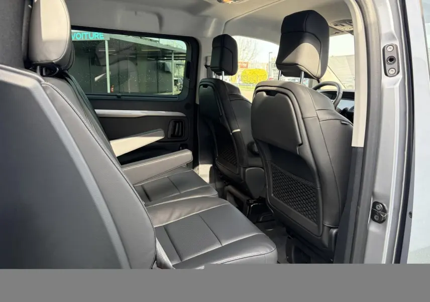 Vue intérieure côté gauche du Citroën Jumpy gris acier, montrant la banquette arrière en cuir et les sièges avant noirs.