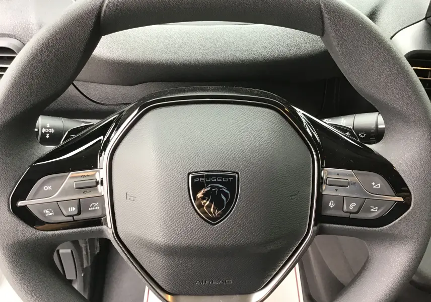 Vue rapprochée du volant noir du Peugeot Partner XL 2026 avec commandes intégrées et logo lion central.
