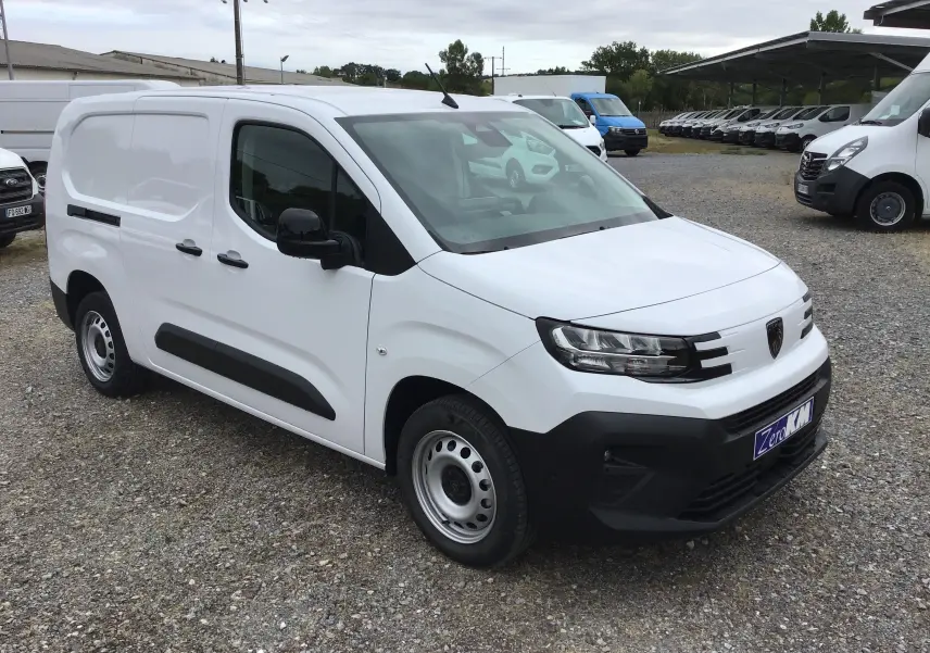 Peugeot Partner blanc en 3/4 avant droit sur parking, avec protections noires latérales et calandre moderne.