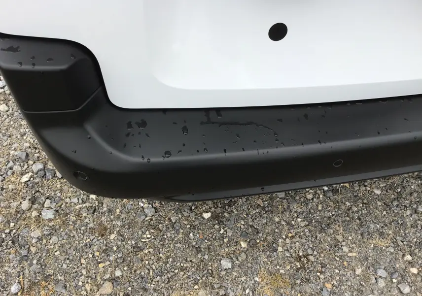 Gros plan sur le pare-chocs arrière noir du Peugeot Partner XL blanc, avec capteurs de recul visibles et traces d'eau.