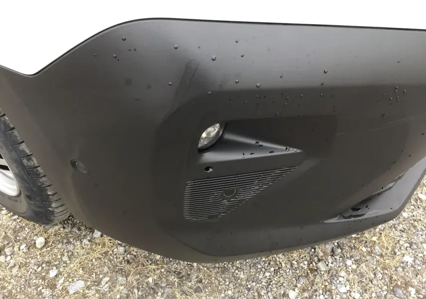 Gros plan sur le pare-chocs avant droit noir du Peugeot Partner blanc, avec antibrouillard et capteur de stationnement visible.
