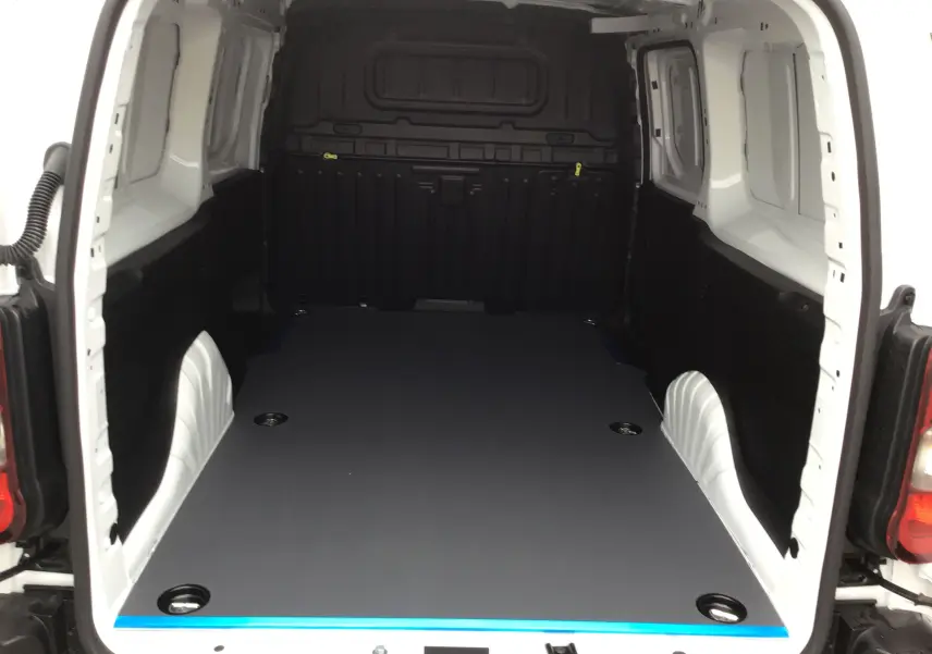 Vue arrière du Peugeot Partner blanc montrant l’espace de chargement avec plancher antidérapant et parois noires.