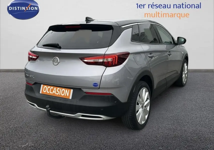 Opel Grandland X gris clair vu en 3/4 arrière droit, avec attelage et jantes alliage 19 pouces visibles.