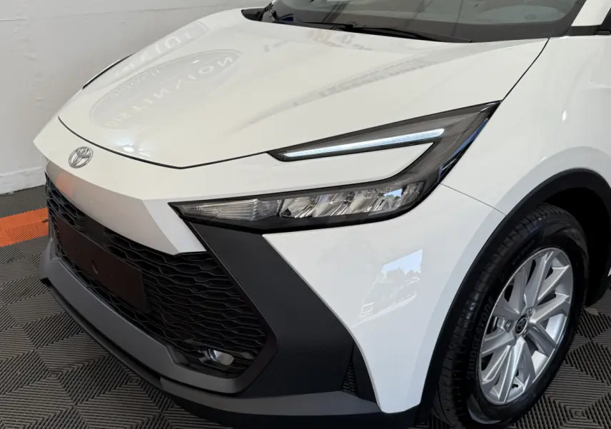 Vue 3/4 avant droit du Toyota C-HR 1.8 Hybride 140 Dynamic blanc avec phares LED et calandre noire texturée.