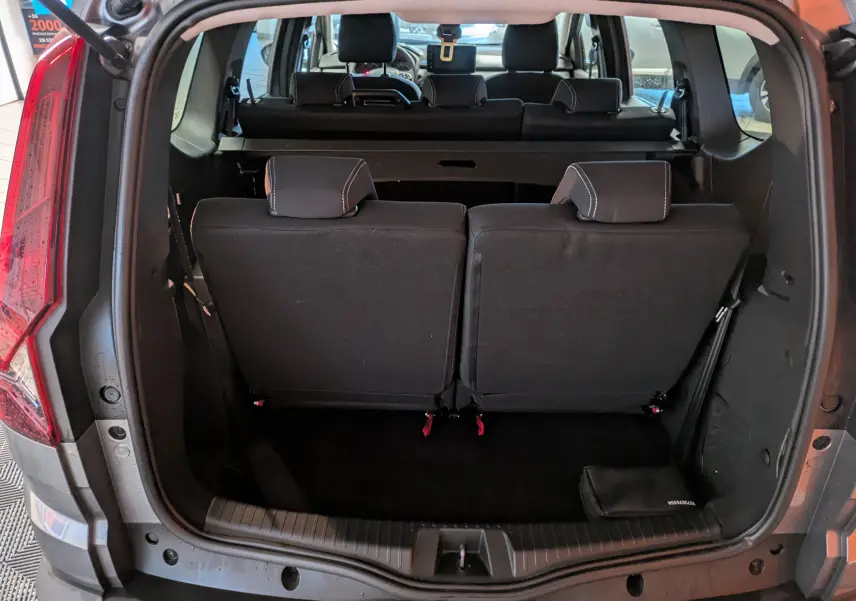 Vue arrière du coffre ouvert du Dacia Jogger gris schiste métal, montrant les sièges arrière rabattus et l’espace de chargement.