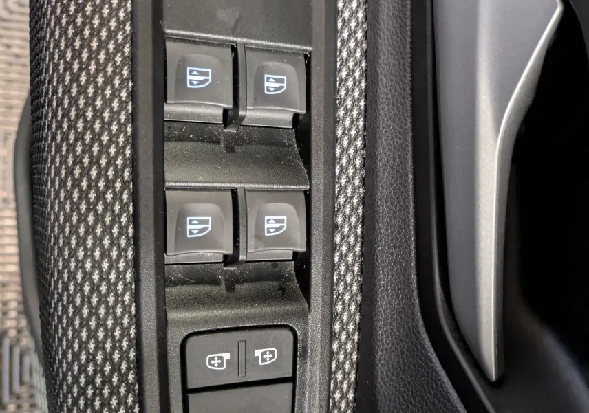 Gros plan sur les commandes des vitres électriques et réglages des rétroviseurs côté conducteur du Dacia Jogger gris schiste.