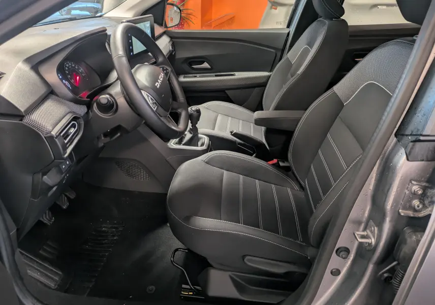 Vue intérieure côté conducteur du Dacia Jogger gris schiste, montrant les sièges noirs, le volant et la boîte manuelle.