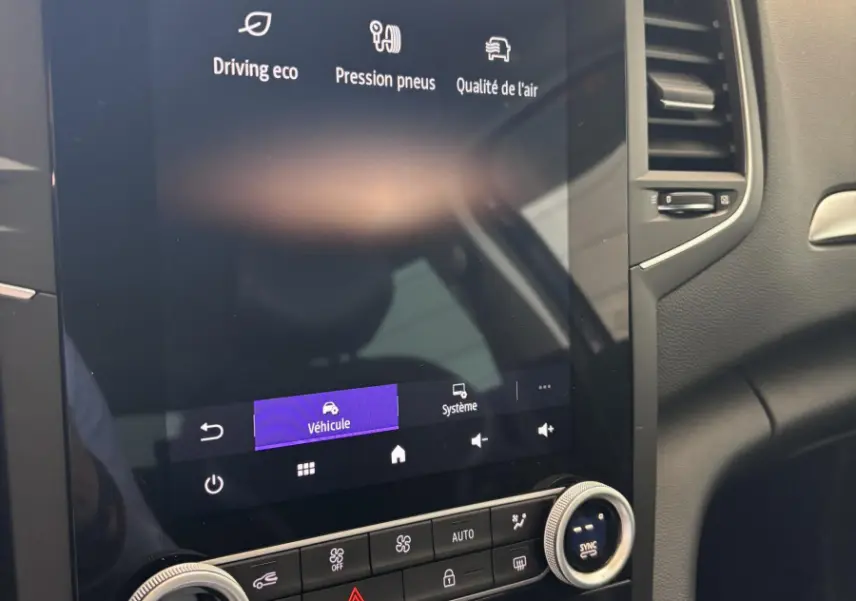 Vue rapprochée de l'écran tactile central et des commandes de climatisation dans l'habitacle noir de la Renault Mégane bleu 2023.