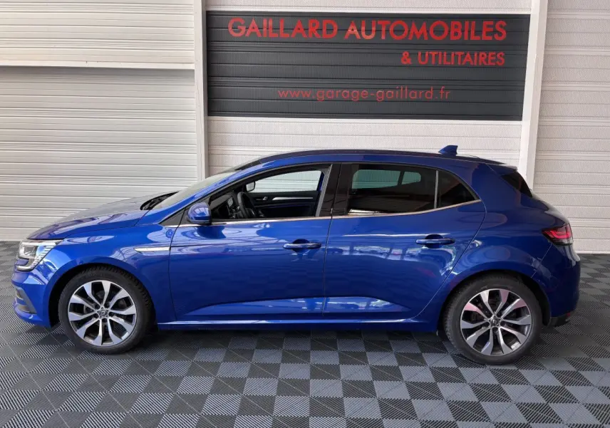 Profil côté gauche de la Renault Mégane bleu 2023 avec jantes alliage et vitres teintées, en intérieur showroom.