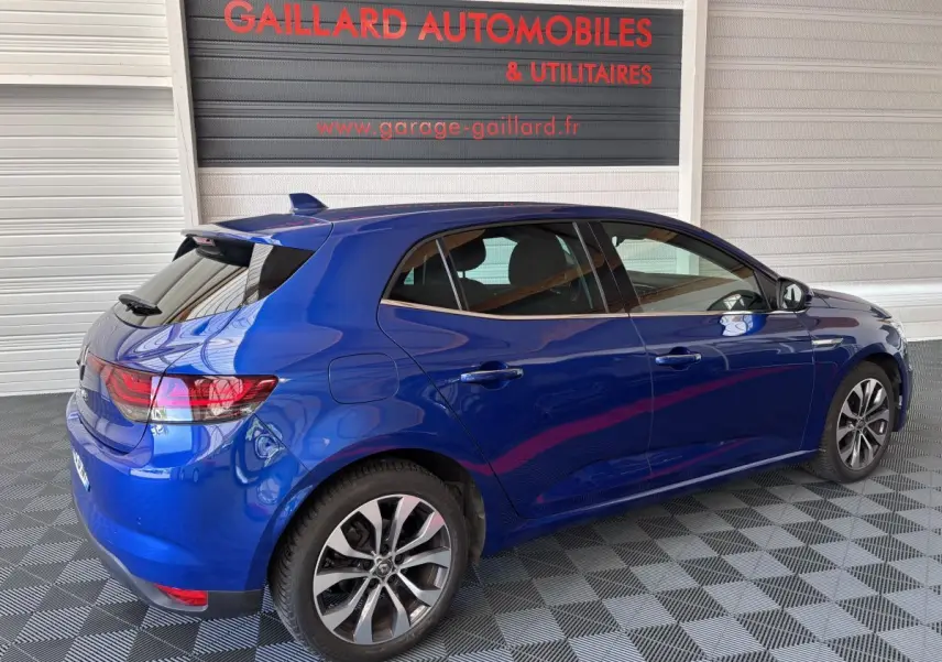 Renault Mégane bleu vue 3/4 arrière côté droit, avec vitres teintées et jantes alliage, en intérieur garage.